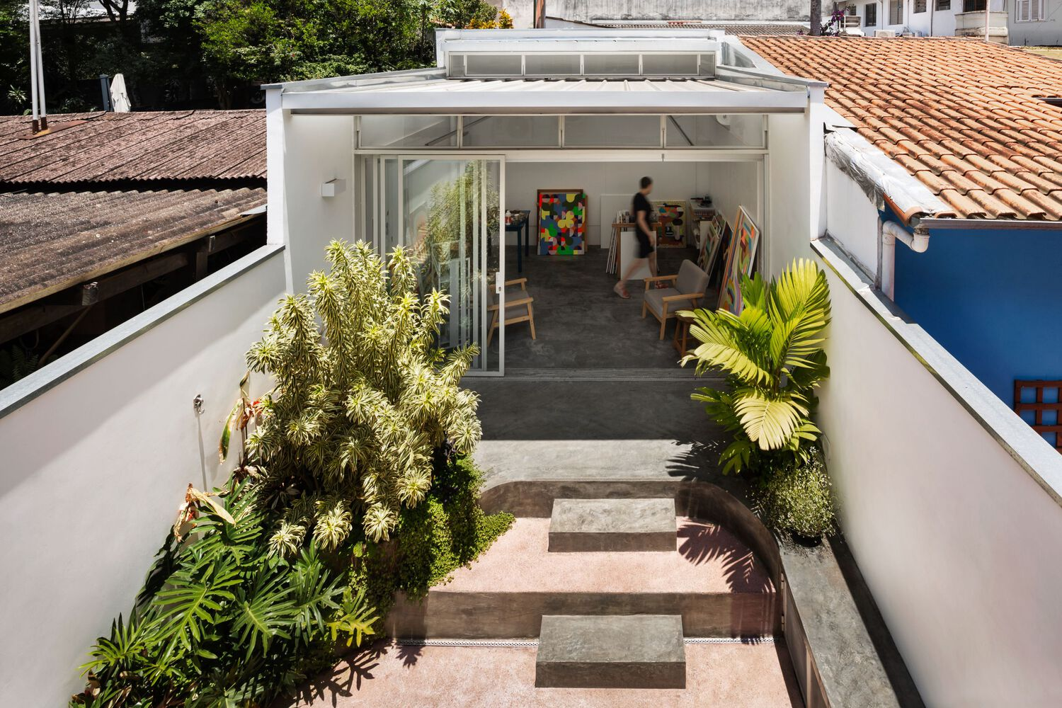 Aerial view: the atelier volume with translucent roof between the existing terracotta-roofed house and courtyard garden