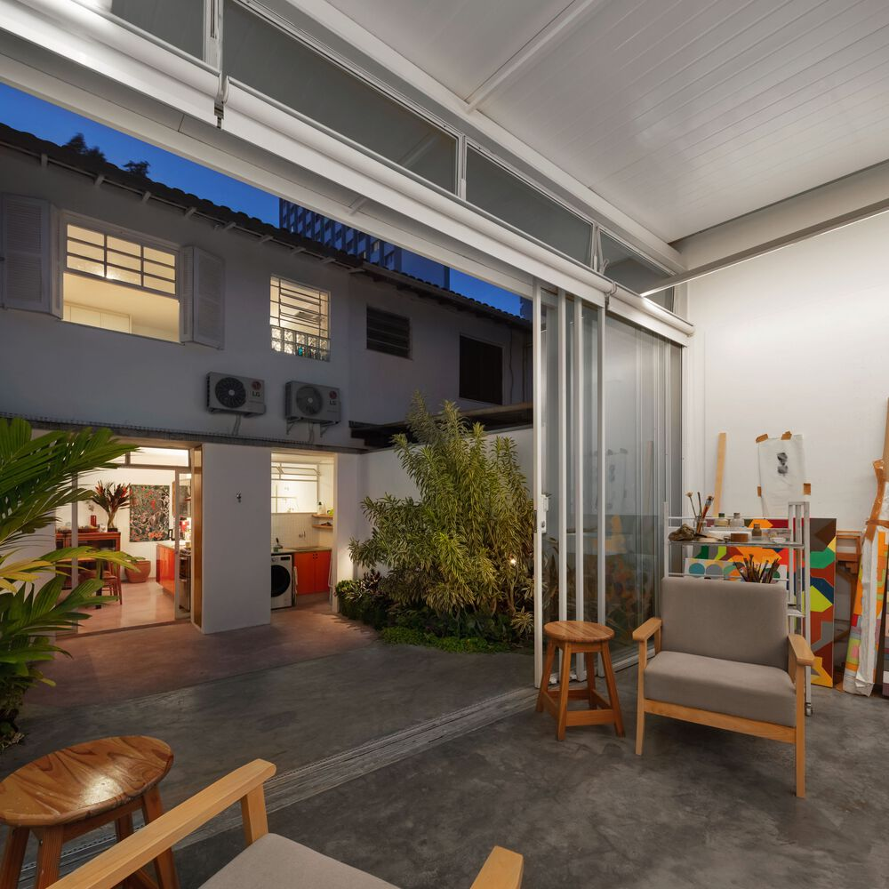 Dusk from the atelier: glass walls open, paintings visible, steel frame and translucent roof lit from inside