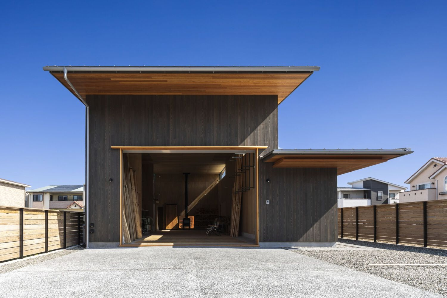 Entry facade with dark vertical timber cladding and overhanging eaves against a clear blue sky