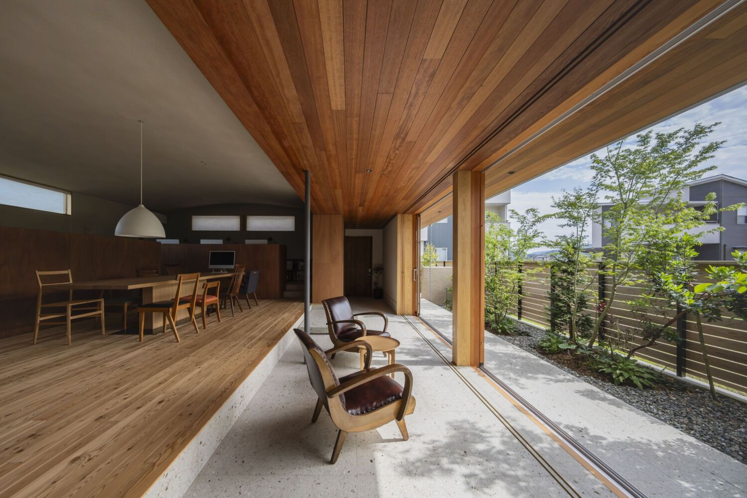 Open-plan interior with slatted timber ceiling and sliding doors opening to a planted terrace