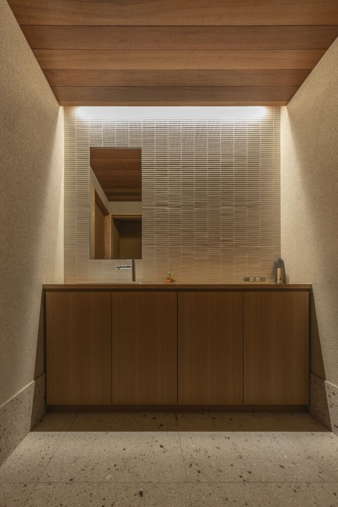Powder room vanity with timber cabinetry beneath a horizontal tile wall lit by concealed perimeter lighting