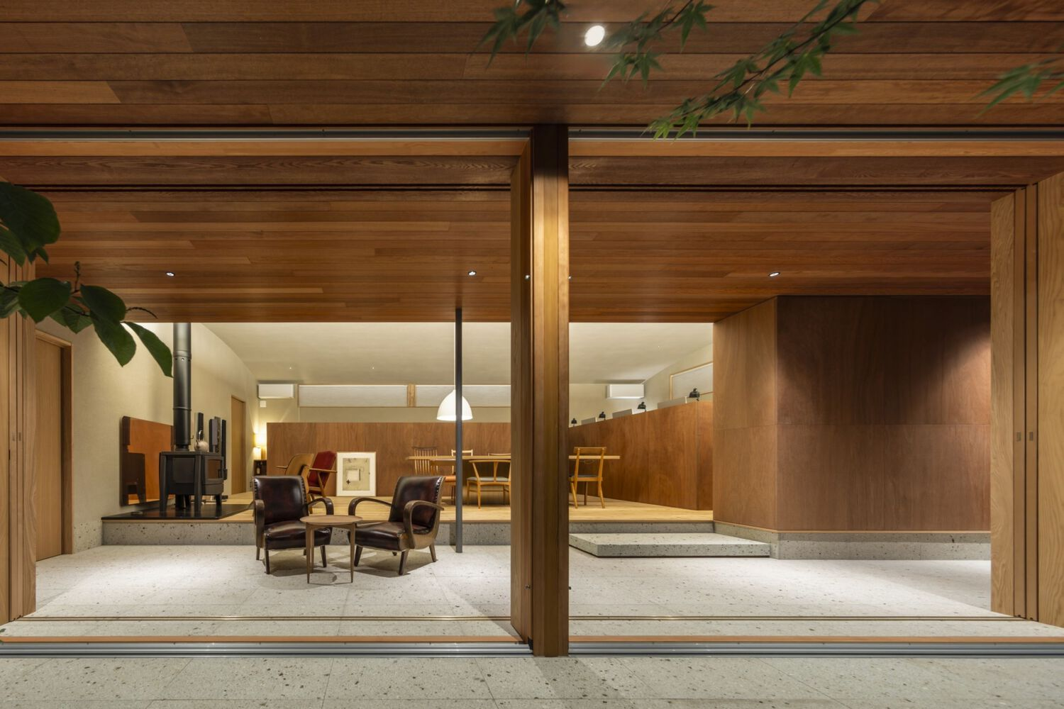 Covered porch with timber columns and ceiling opening onto a warmly lit living room at dusk