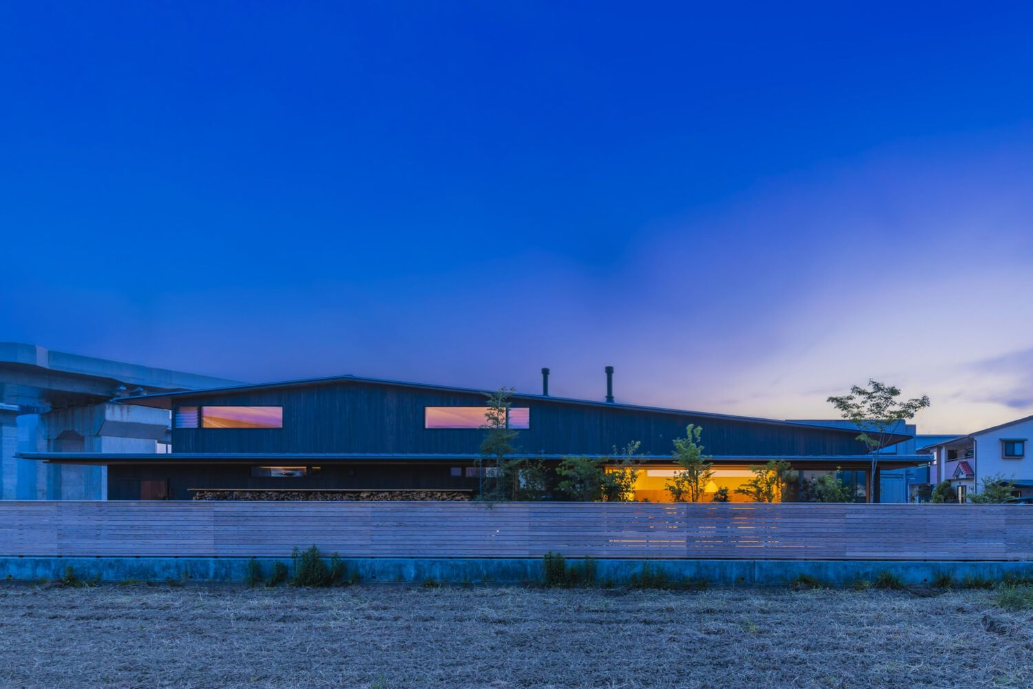 Horizontal dark facade with uplighting along planted bed under a blue twilight sky