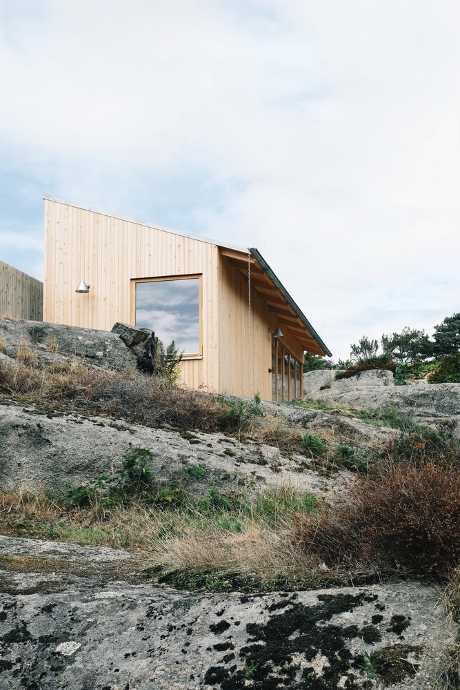 Vertical timber cladding and sloped metal roof nestled into rocky outcrop with scattered vegetation