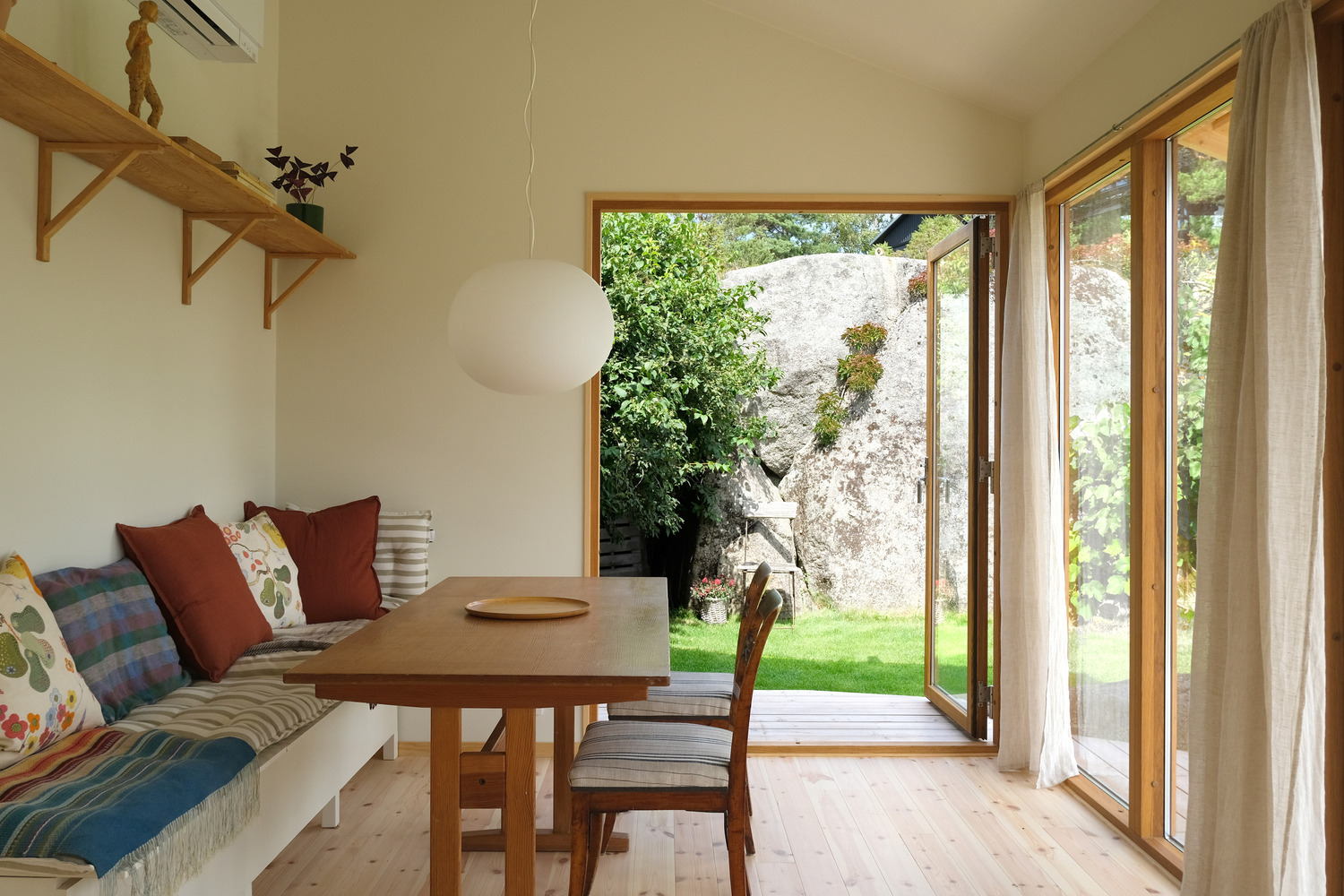 Dining area with built-in bench seating looking out through glazed doors to a weathered stone boulder