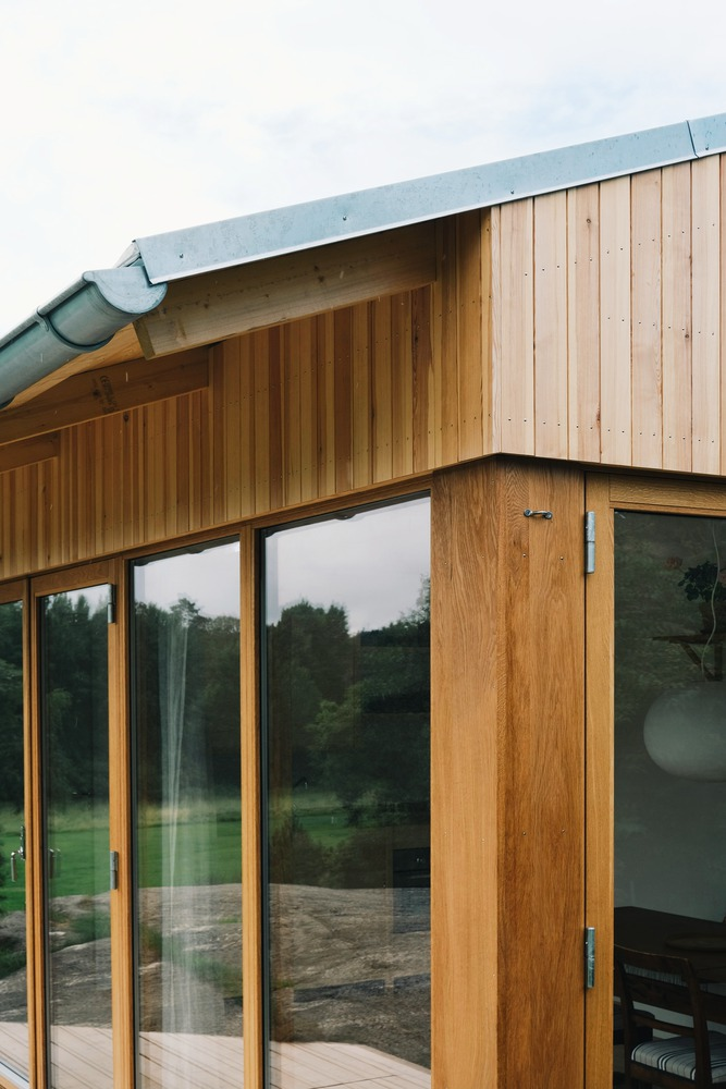 Close-up of the zinc-clad eave edge meeting vertical timber cladding and a glass corner
