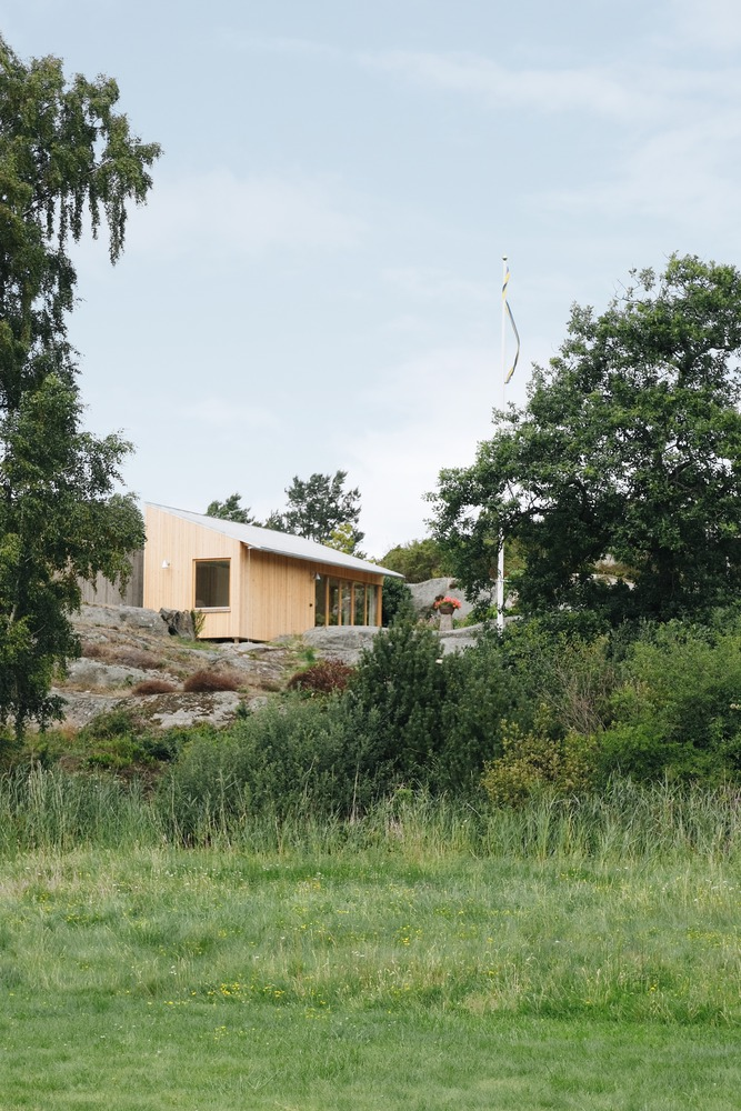 Timber-clad volume with sloping roof set among rocky outcrops and mature trees in a field