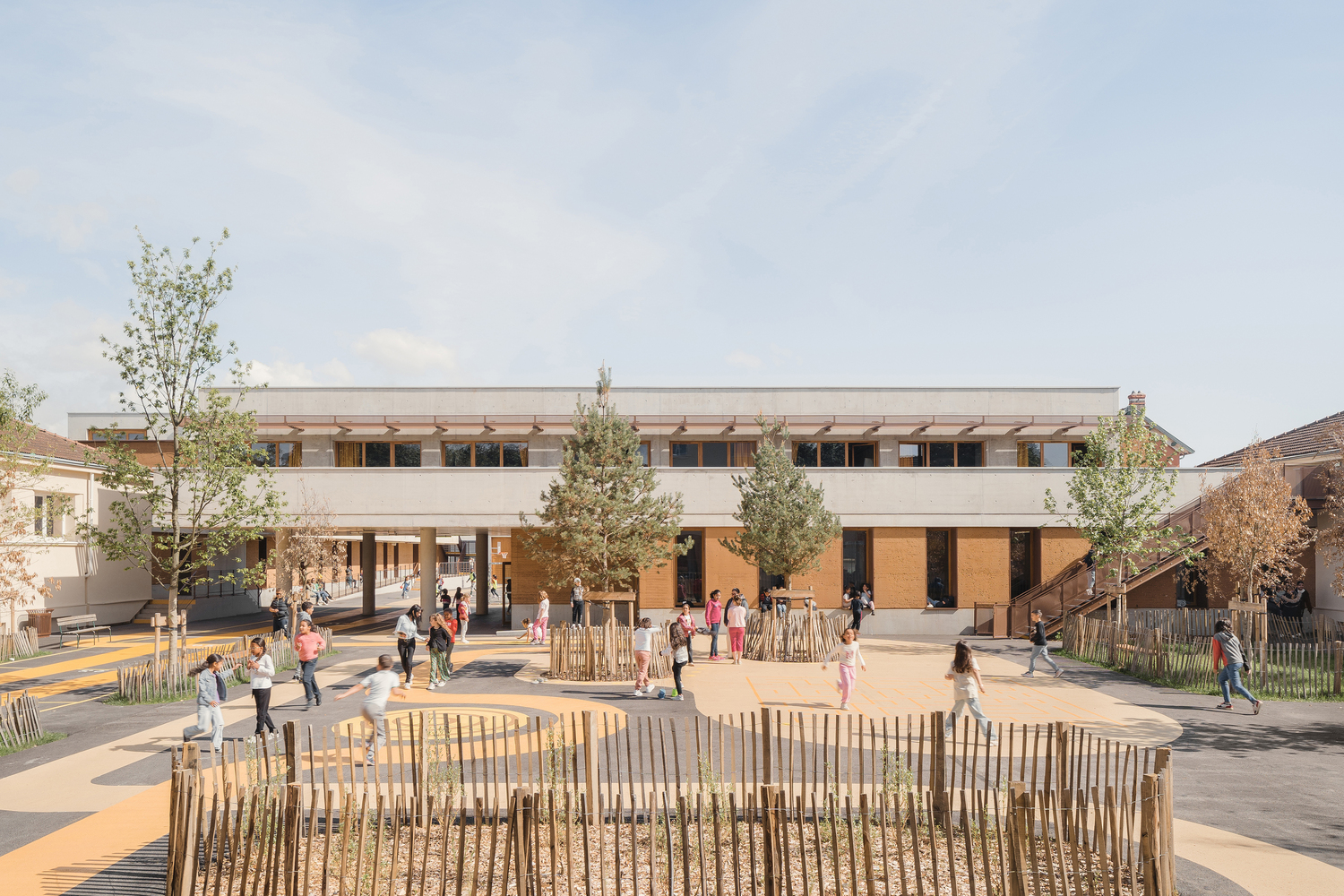 Playground courtyard: two-storey rammed earth and concrete building, timber pergola above, children playing, timber fence playground, young trees