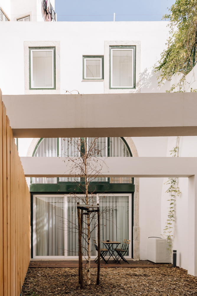 Courtyard with white horizontal beams framing a young tree and gravel ground
