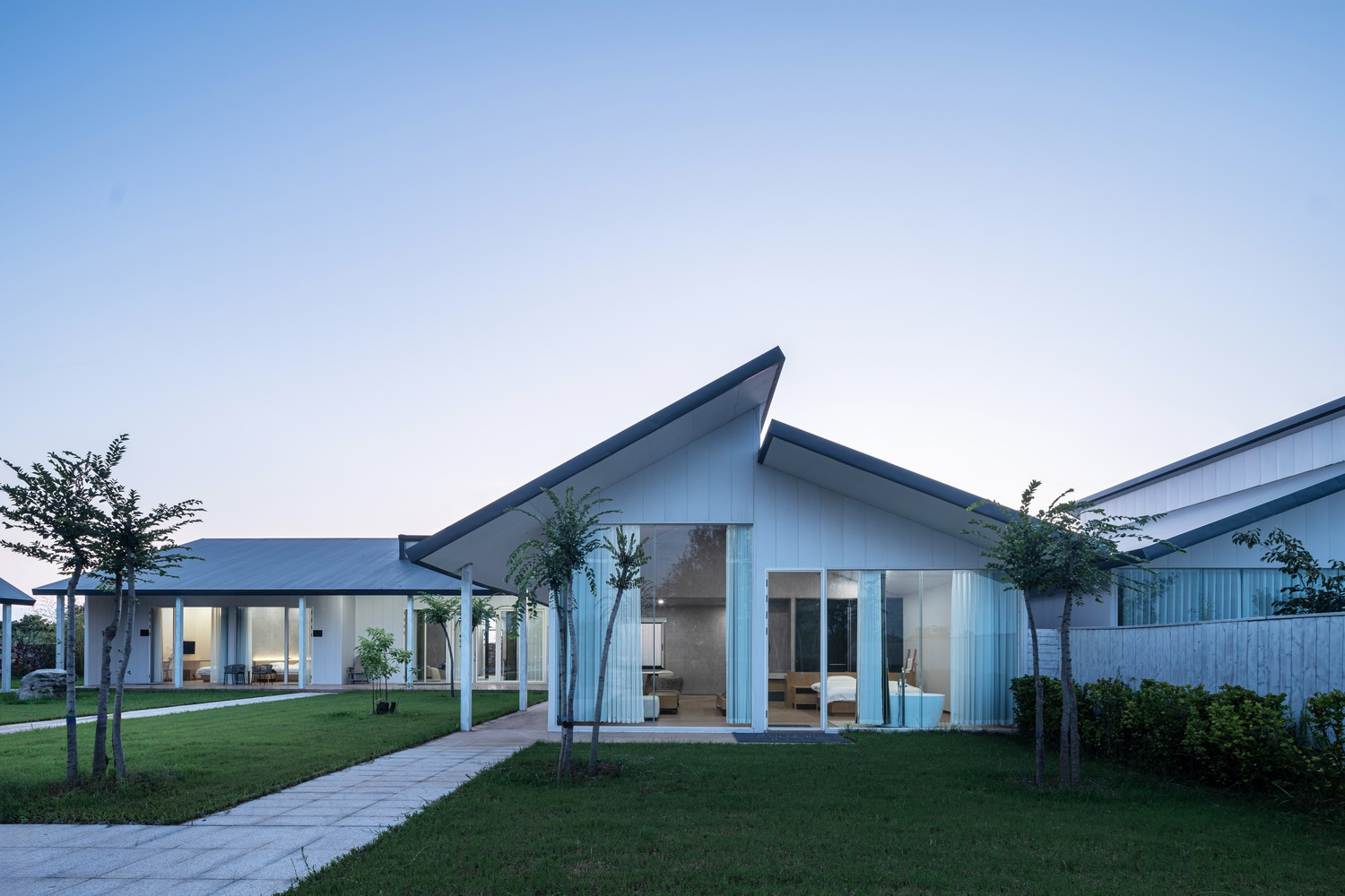 White corrugated metal pavilion with angled gabled roof and glazed entrance at dusk