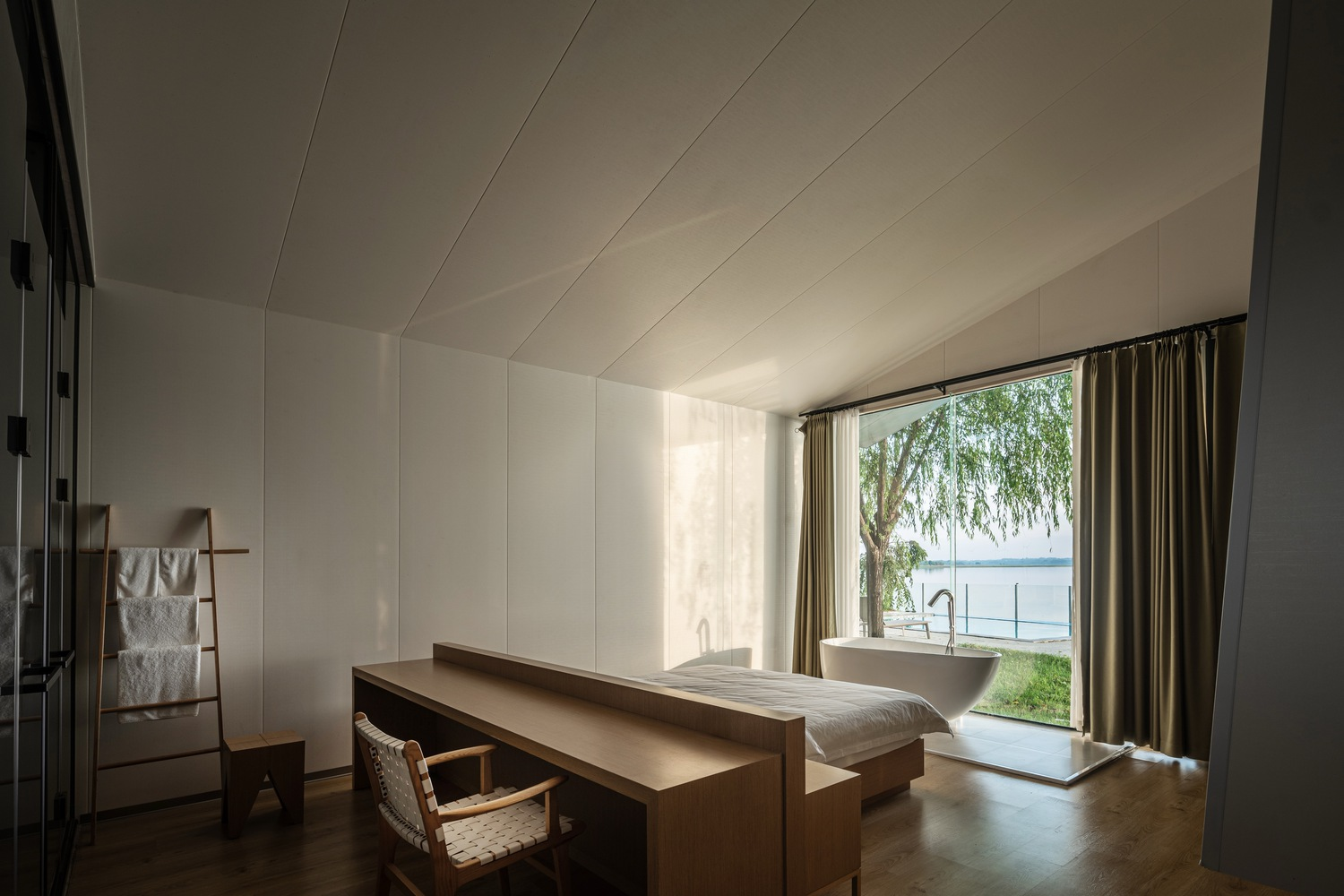 Bedroom interior with paneled ceiling and timber desk facing a full-height window overlooking water