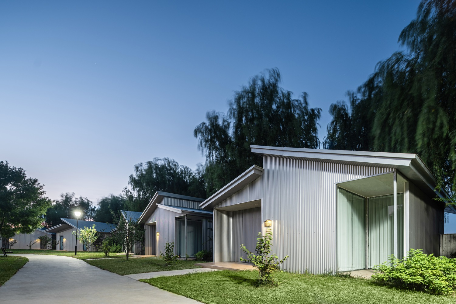 Ribbed metal facade with overhanging eaves and young trees in twilight