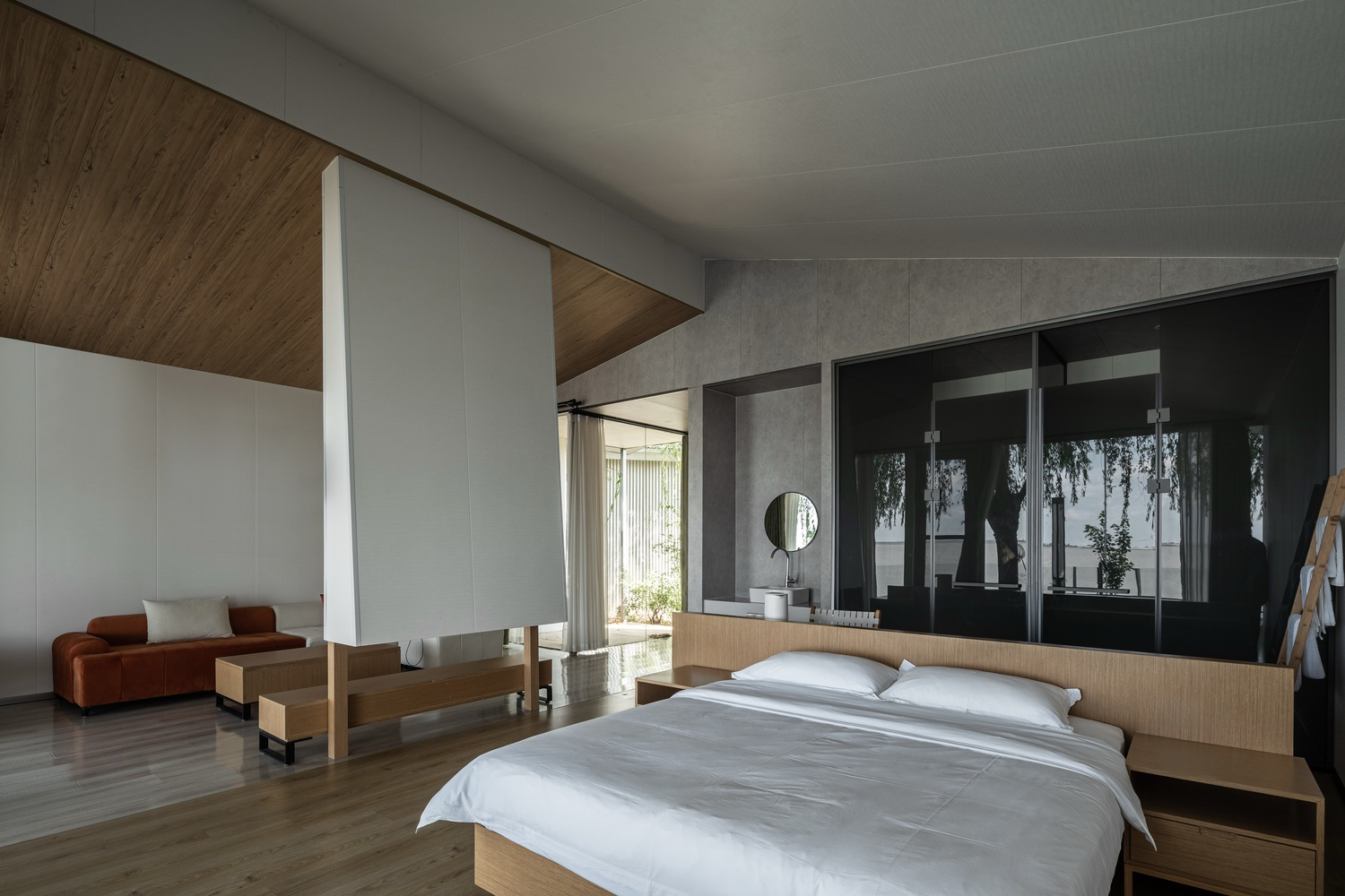 Bedroom with timber ceiling insert, concrete walls, and black framed glazing reflecting garden foliage