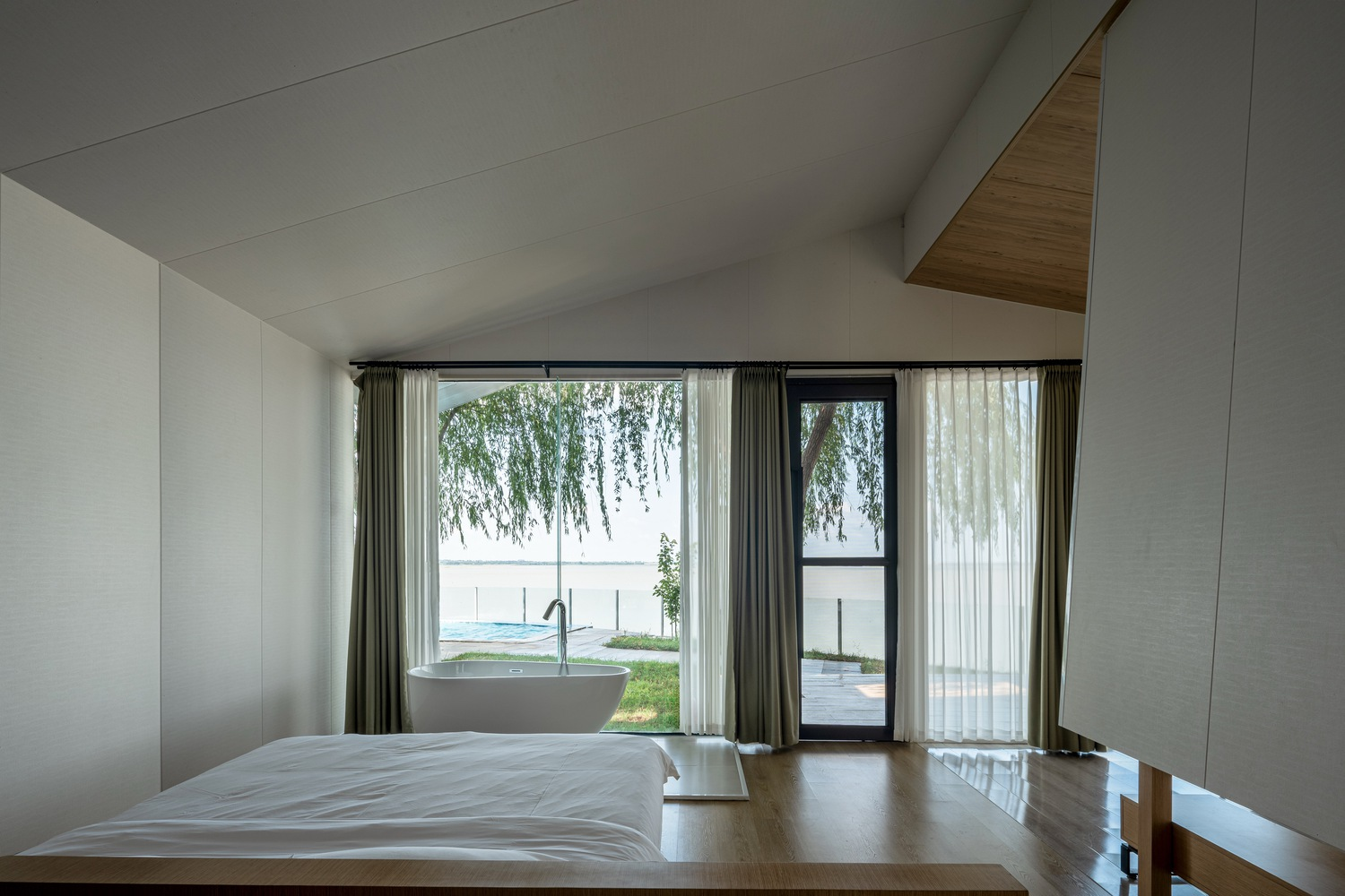 Sleeping loft with freestanding tub visible through window beneath willow branches outside