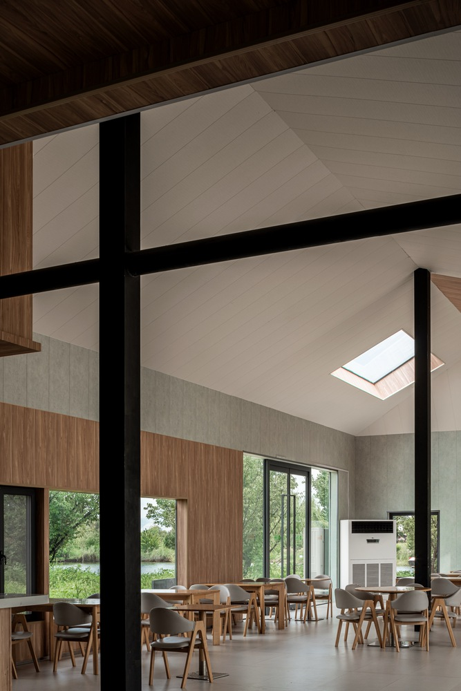Double-height dining hall with exposed black steel columns and skylights above timber-clad walls