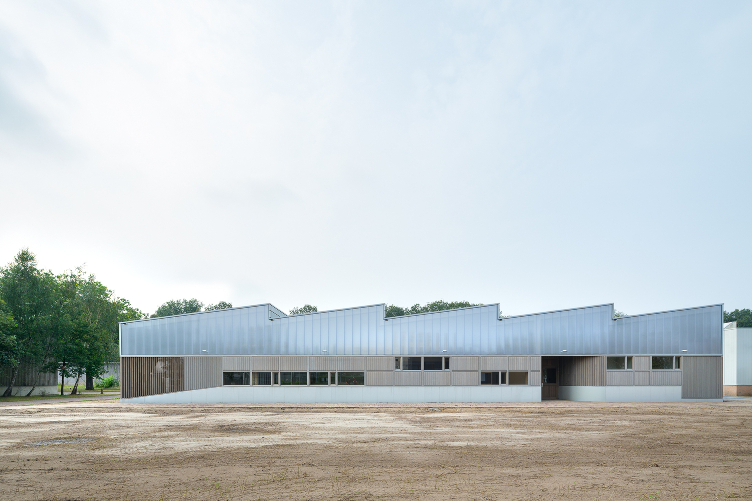 Full exterior view: polycarbonate and timber warehouse with sawtooth roof, set within the prison grounds