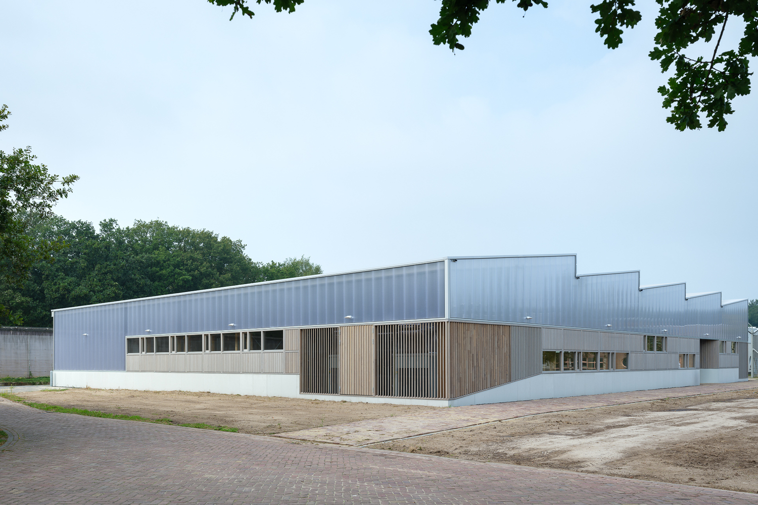 Corner view: the full building length with sawtooth roof profile, timber base, and metal cladding