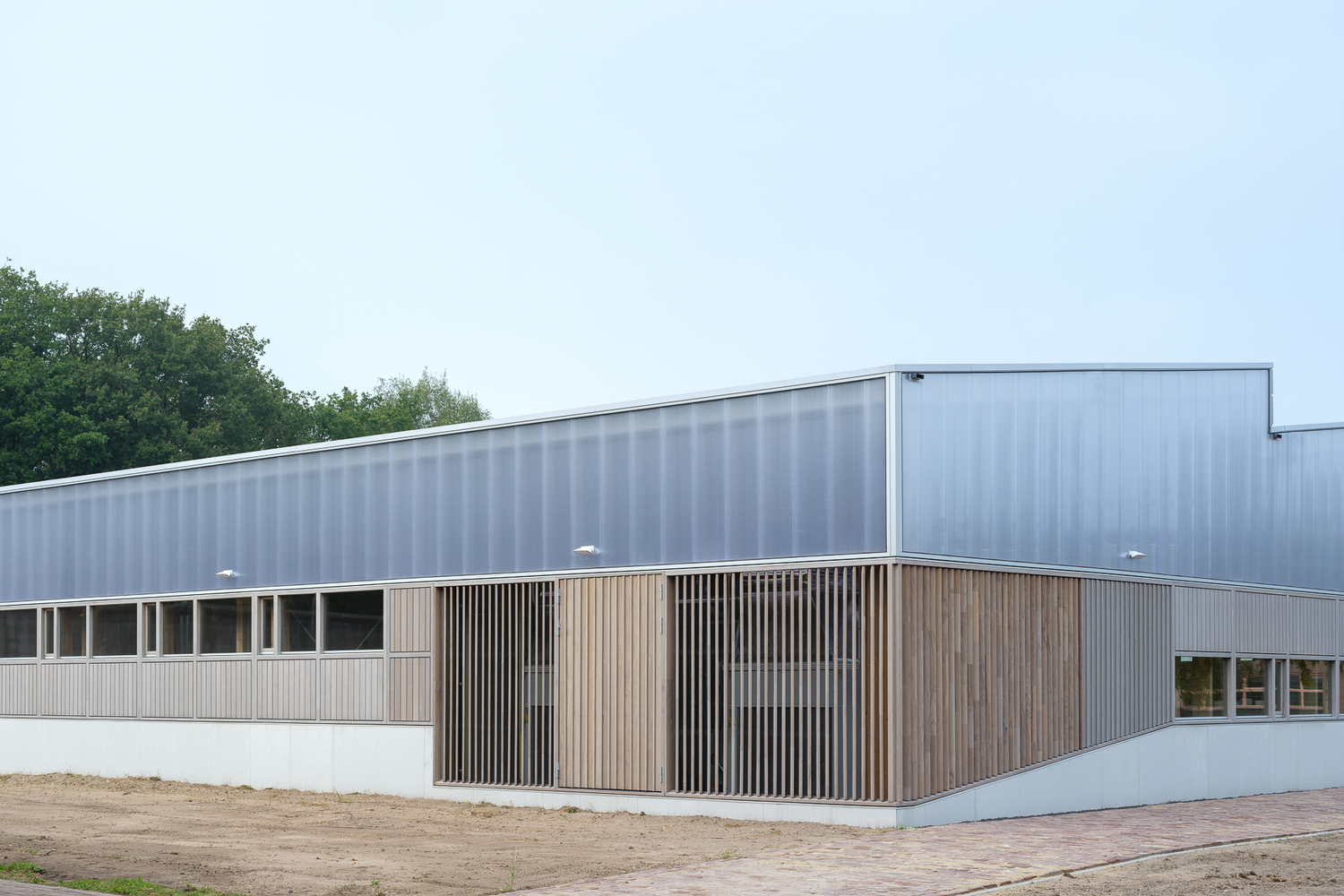 Side elevation: the full building with timber-clad base, sawtooth clerestories, and gravel forecourt
