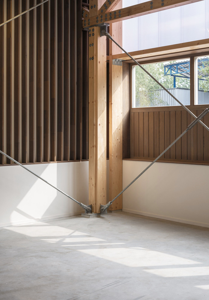 Interior detail: timber column, steel cross-brace, and polycarbonate wall admitting diffused daylight