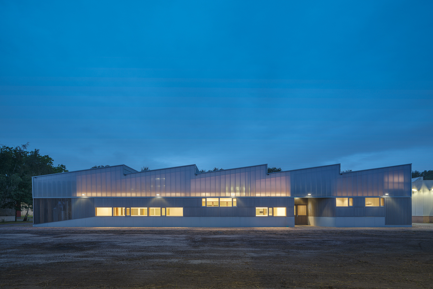 Full exterior at dusk: the warehouse glowing from within, windows lit along the timber base