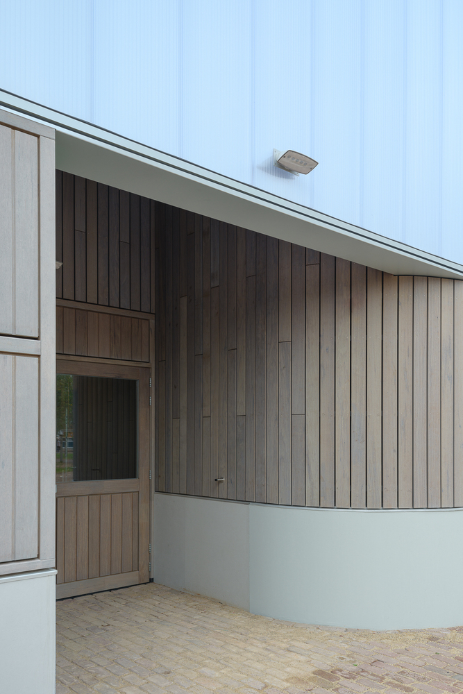 Facade junction: rounded timber-clad corner where the entrance volume meets the main hall