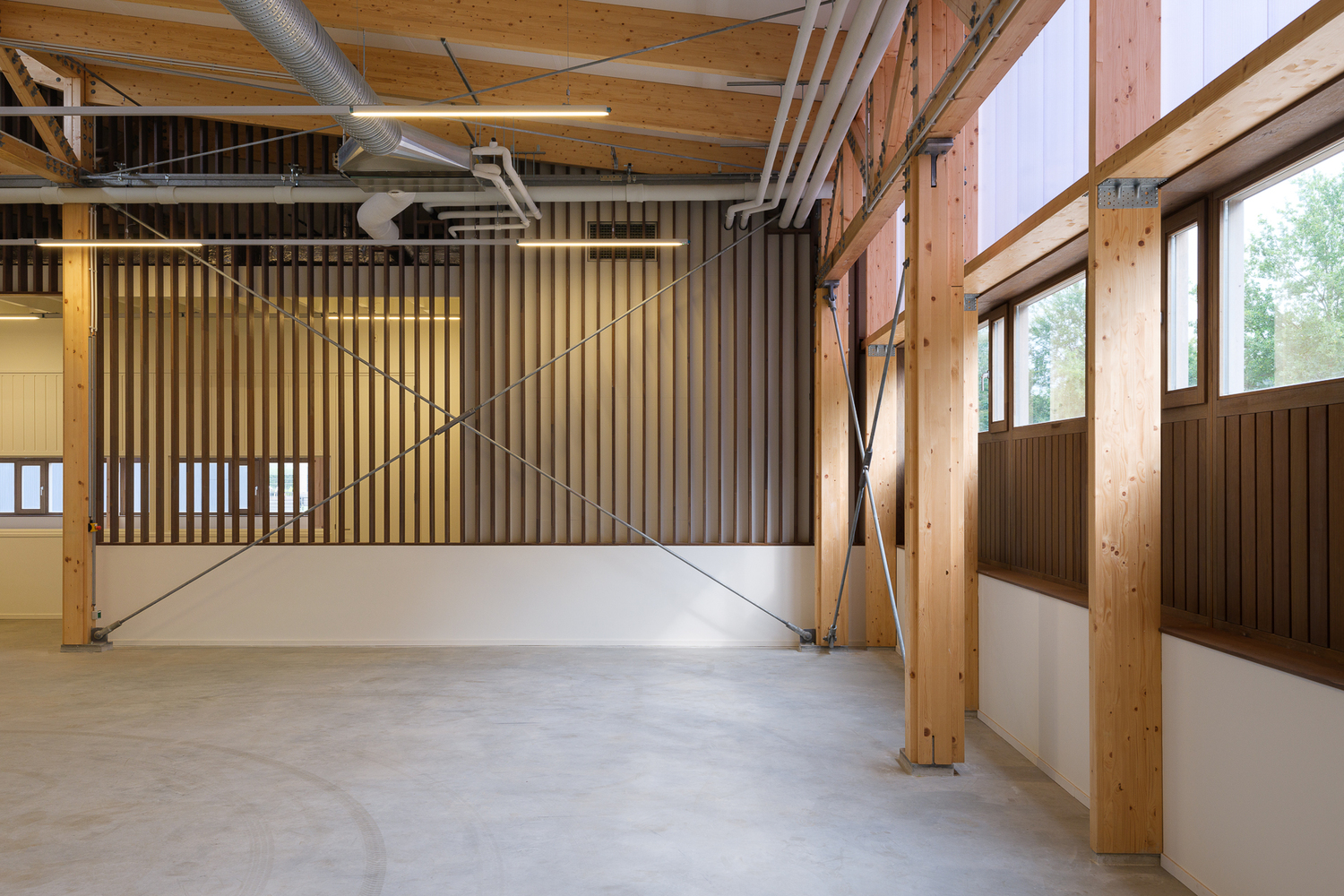 Interior: open workshop hall with timber slatted wall partition, glulam columns, and polished concrete floor