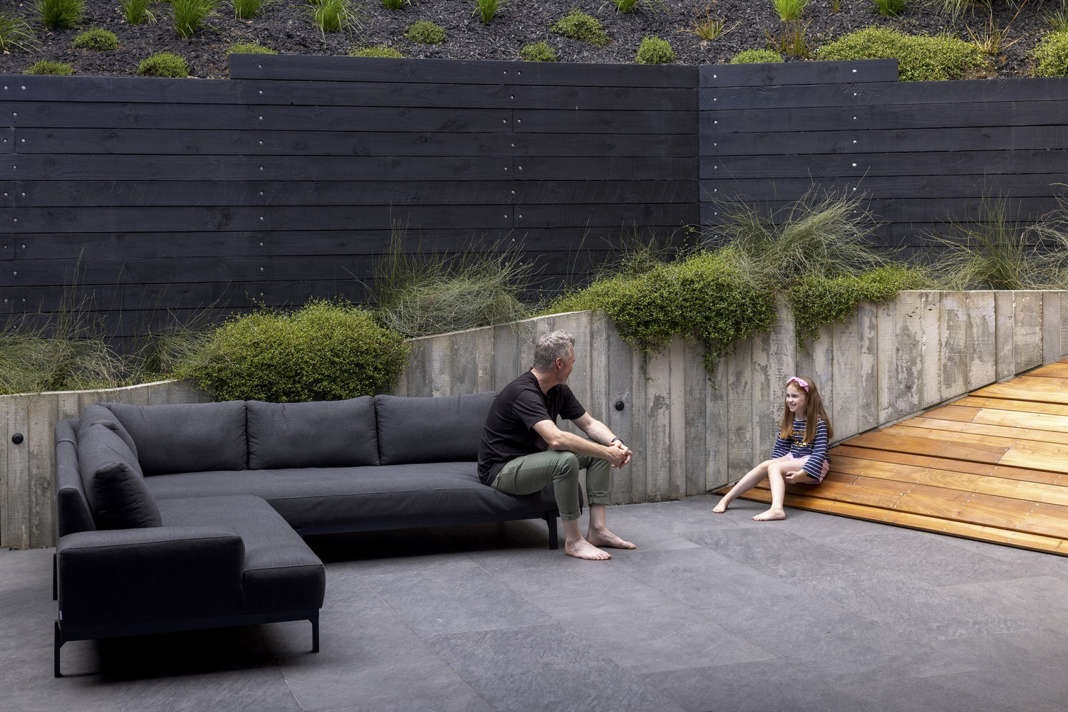 Sunken courtyard with board-formed concrete retaining walls, planted beds, and two figures seated