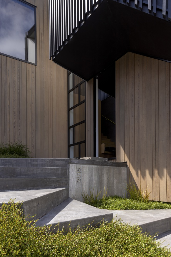 Entry sequence with concrete steps and black steel framed doorway beneath a cantilevered upper volume
