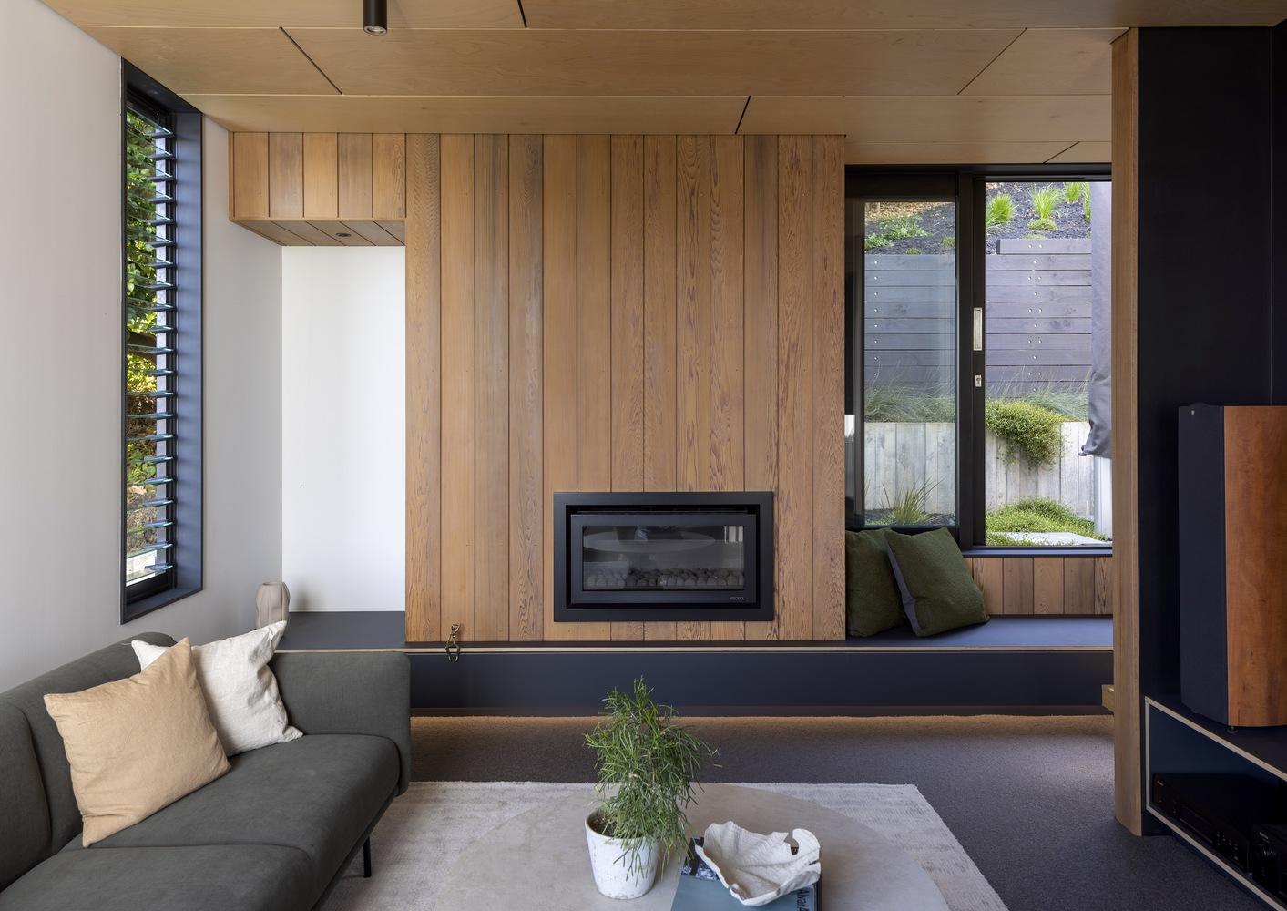 Living room with timber wall concealing a fireplace and built-in window seat with courtyard view
