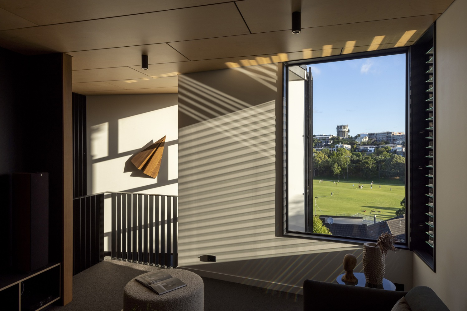 Upper level sitting nook with angled louvered shadows on walls and park views through tall glazing