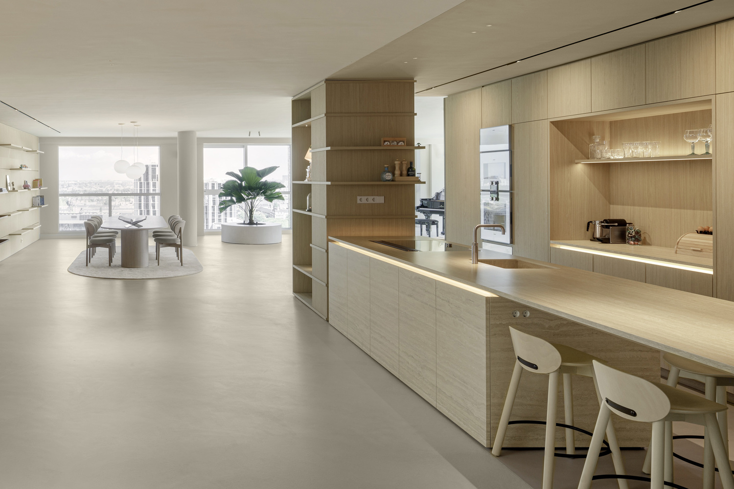 Open kitchen island with light wood cabinetry and integrated shelving leading to dining area beyond