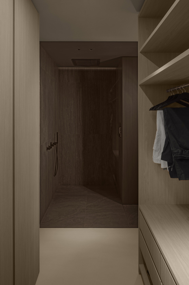 Walk-through shower alcove viewed from a closet with hanging garments and open timber shelving