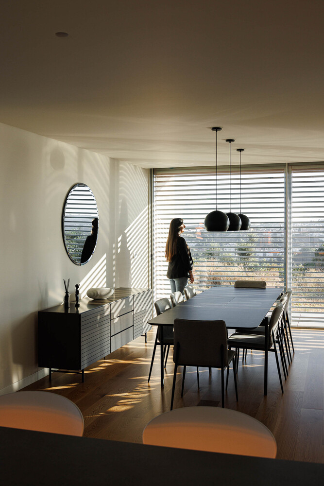 Dining room with striped sunlight patterns from external louvers falling across walls and dark timber floor
