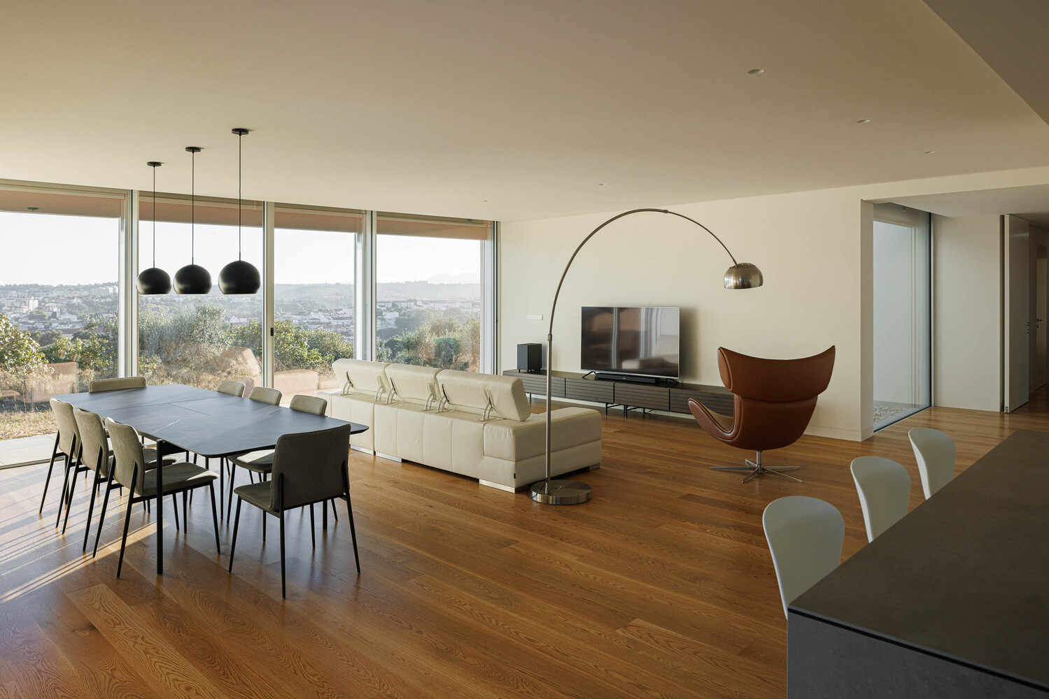 Open-plan living and dining space with wood flooring and full-height glazing overlooking rolling landscape