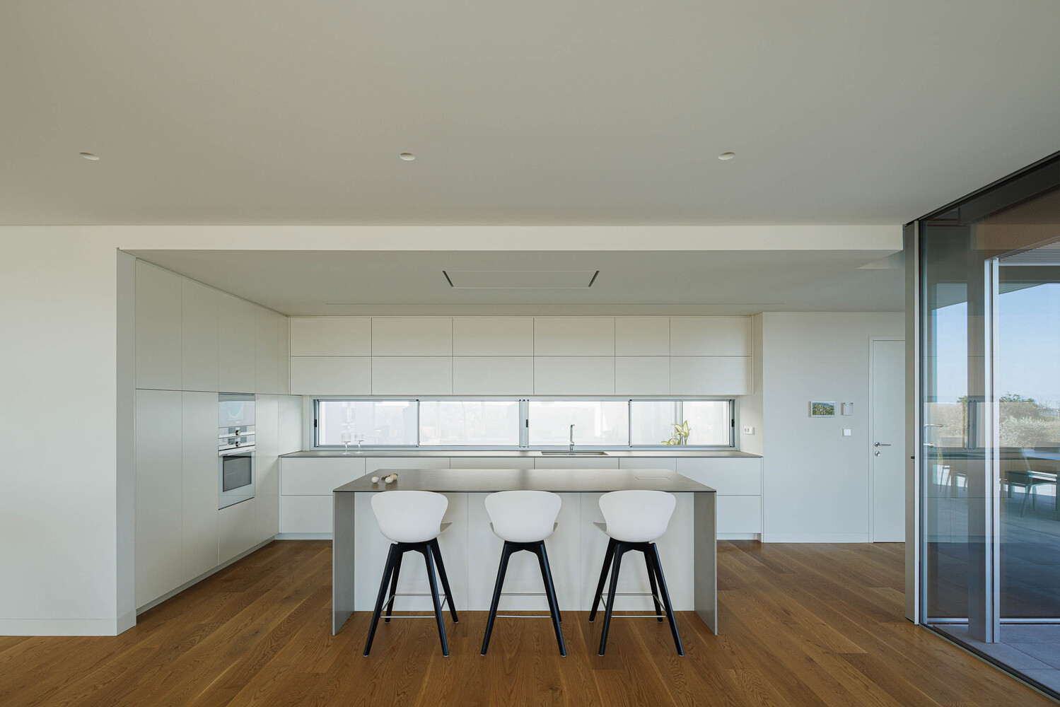White kitchen with island and three stools beneath a horizontal ribbon window