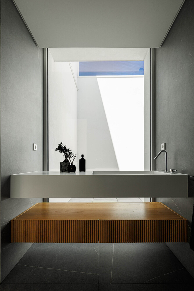 Powder room with floating concrete sink, ribbed timber cabinet below, and skylight framing white walls
