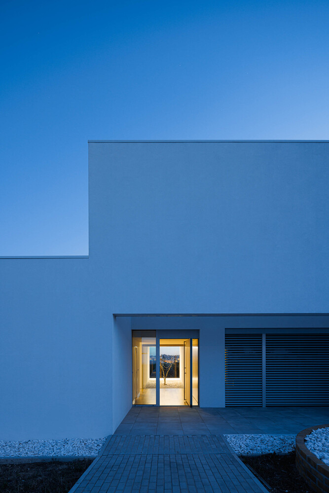 Recessed entry with lit glass door and horizontal louvered panel at twilight