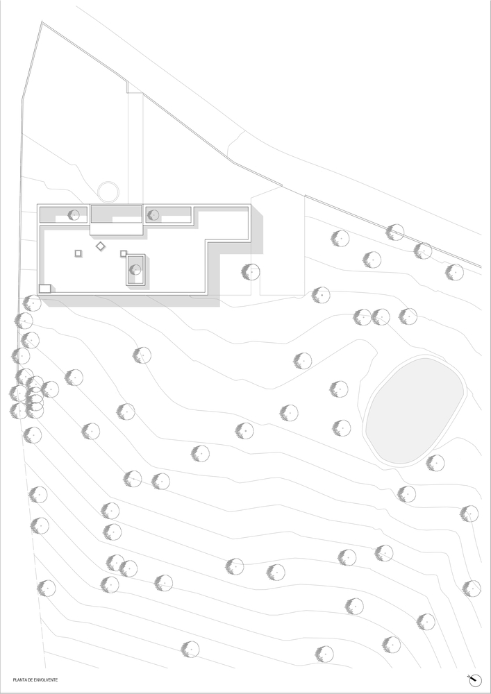 Site plan drawing showing a linear building mass with interior courtyard surrounded by scattered trees on sloping terrain