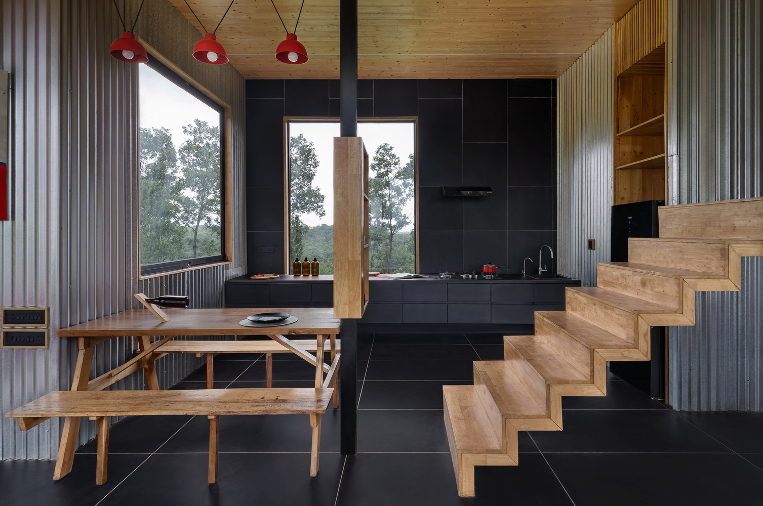 Dining area with timber table and benches beside timber stairs and black tile floor