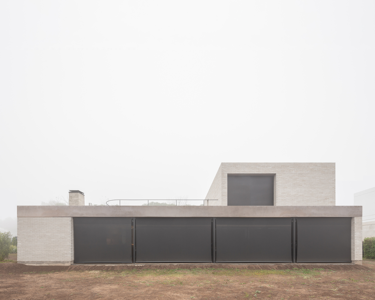 Street facade: opaque two-metre wall with dark steel panels, rooftop terrace above