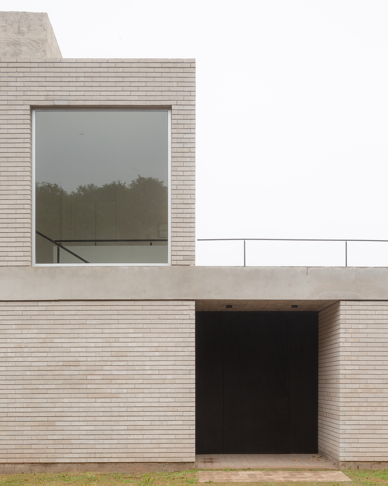 Facade detail: brick volume with large window, steel gate, and concrete lintel