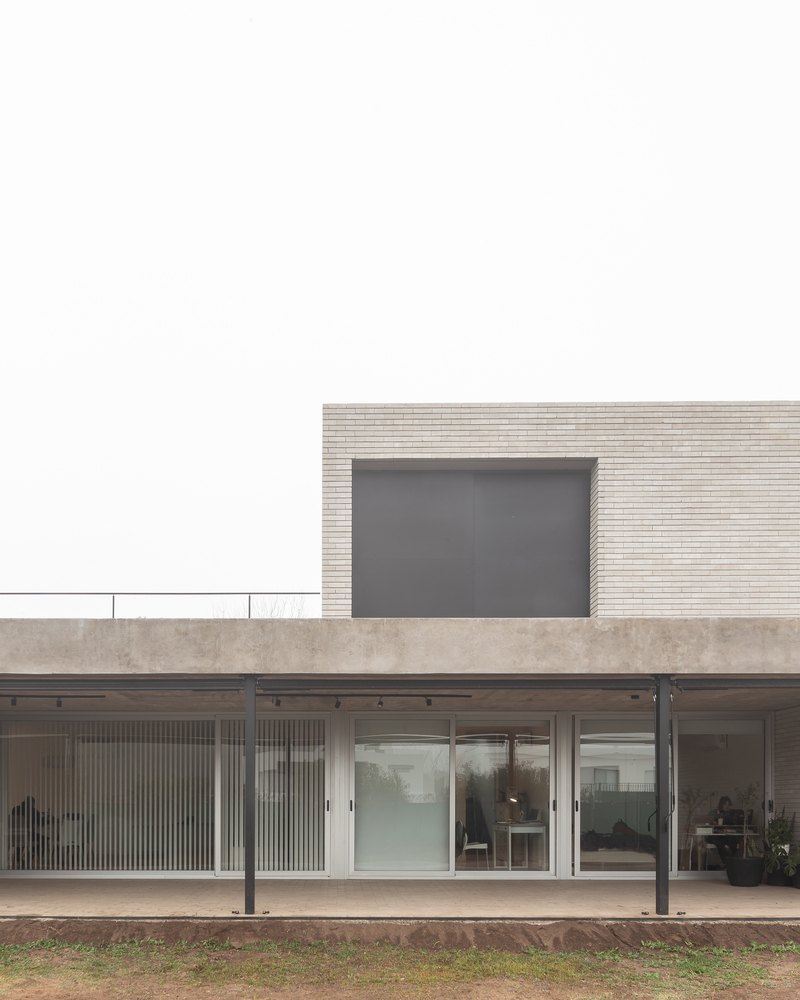Garden elevation: ground-floor glass wall open to the backyard, upper brick volume set back