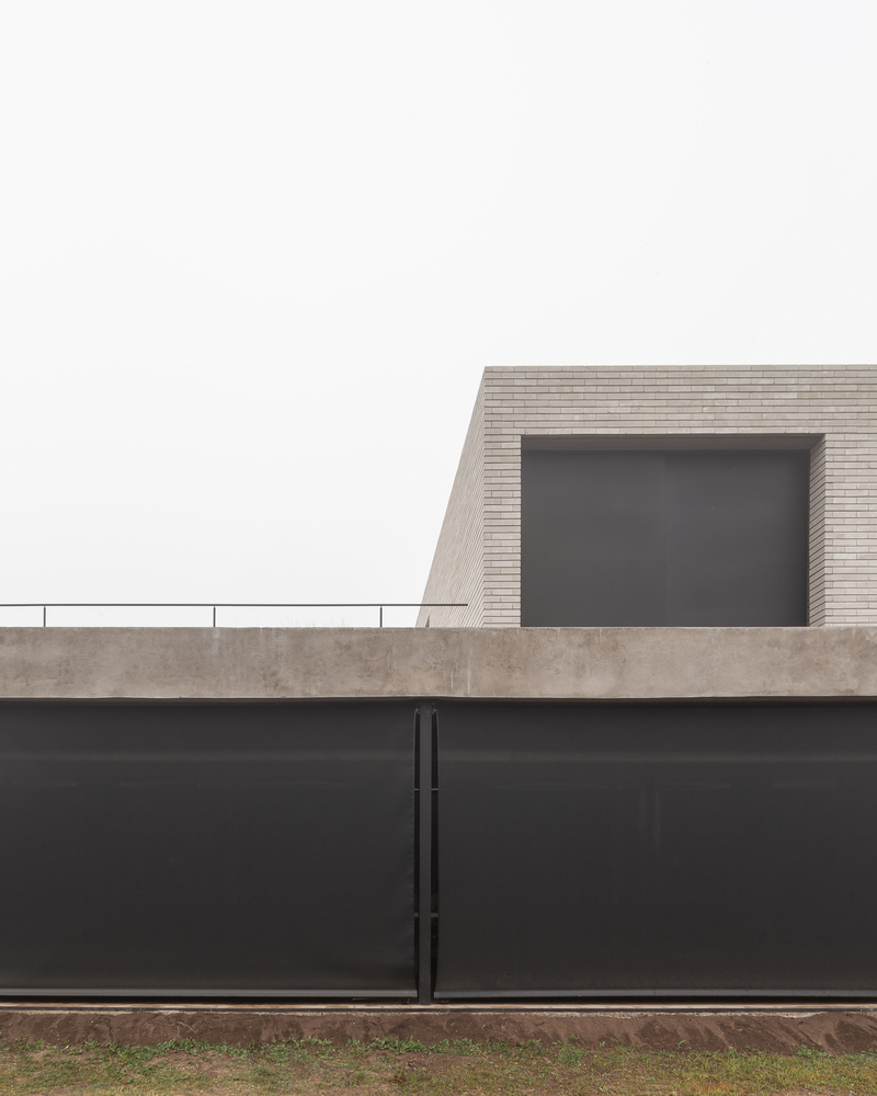 Street boundary: dark steel wall and gate with brick volume and window rising above