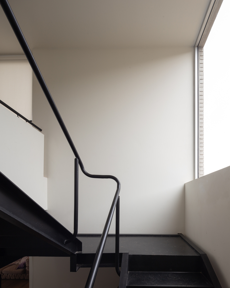Stair detail: black steel stringer and handrail, white walls, clerestory window above