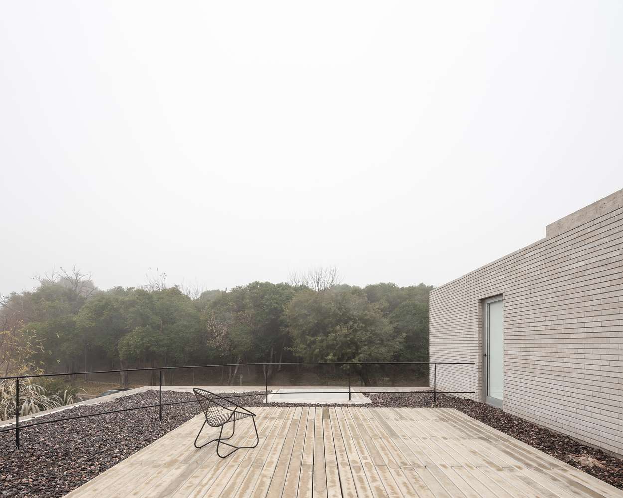 Rooftop terrace: timber deck, wire chair, gravel border, reserve canopy stretching to the horizon