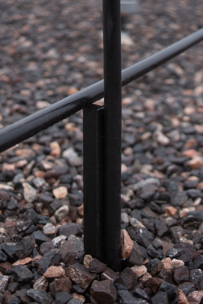 Railing base detail: black steel post meeting gravel on the rooftop terrace