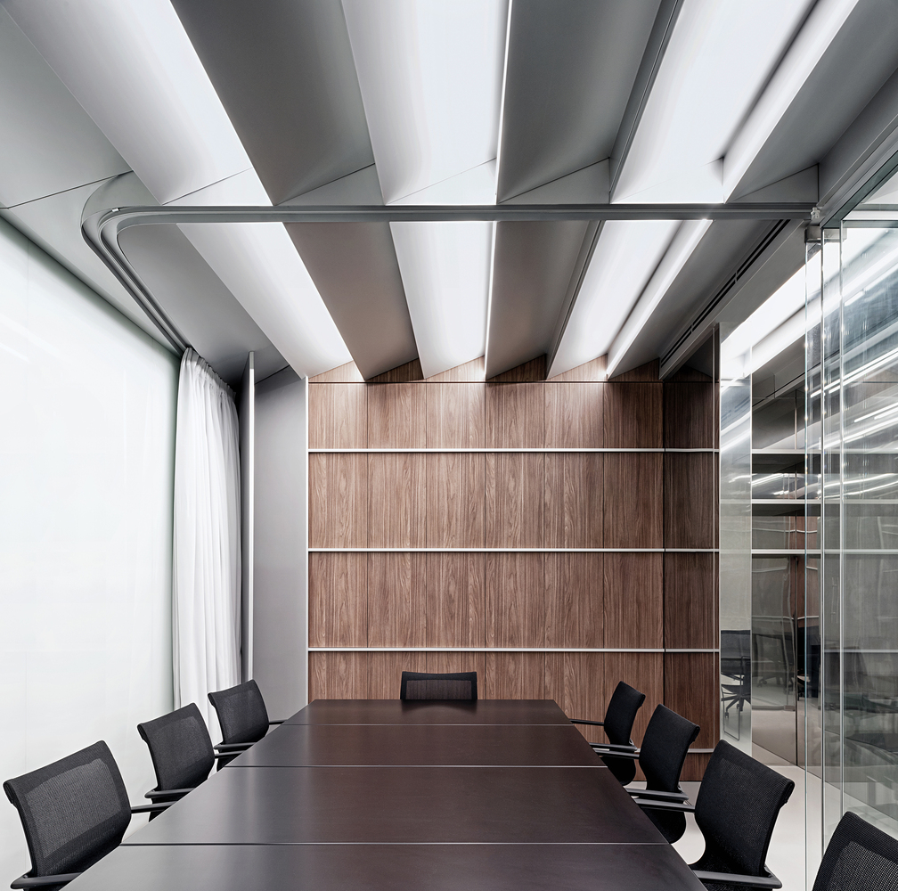 Meeting room: dark table, black mesh chairs, walnut timber wall panel, white ceiling baffles with light strips between