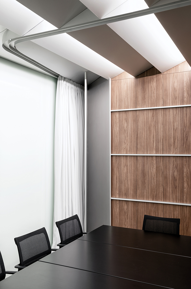 Meeting room corner: walnut panel wall, curtain, black desk, white ceiling baffles casting even light