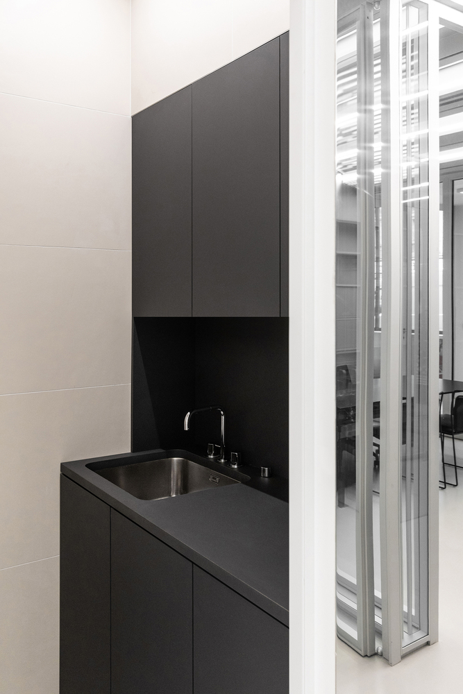 Kitchenette: all-black cabinets and counter with stainless steel sink, glass partition edge visible