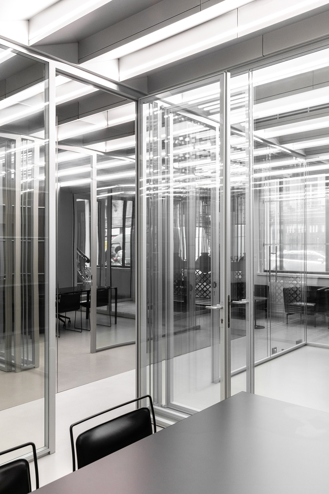 Glass partitions: multiple layers reflecting and overlapping, steel frames, meeting chairs visible through